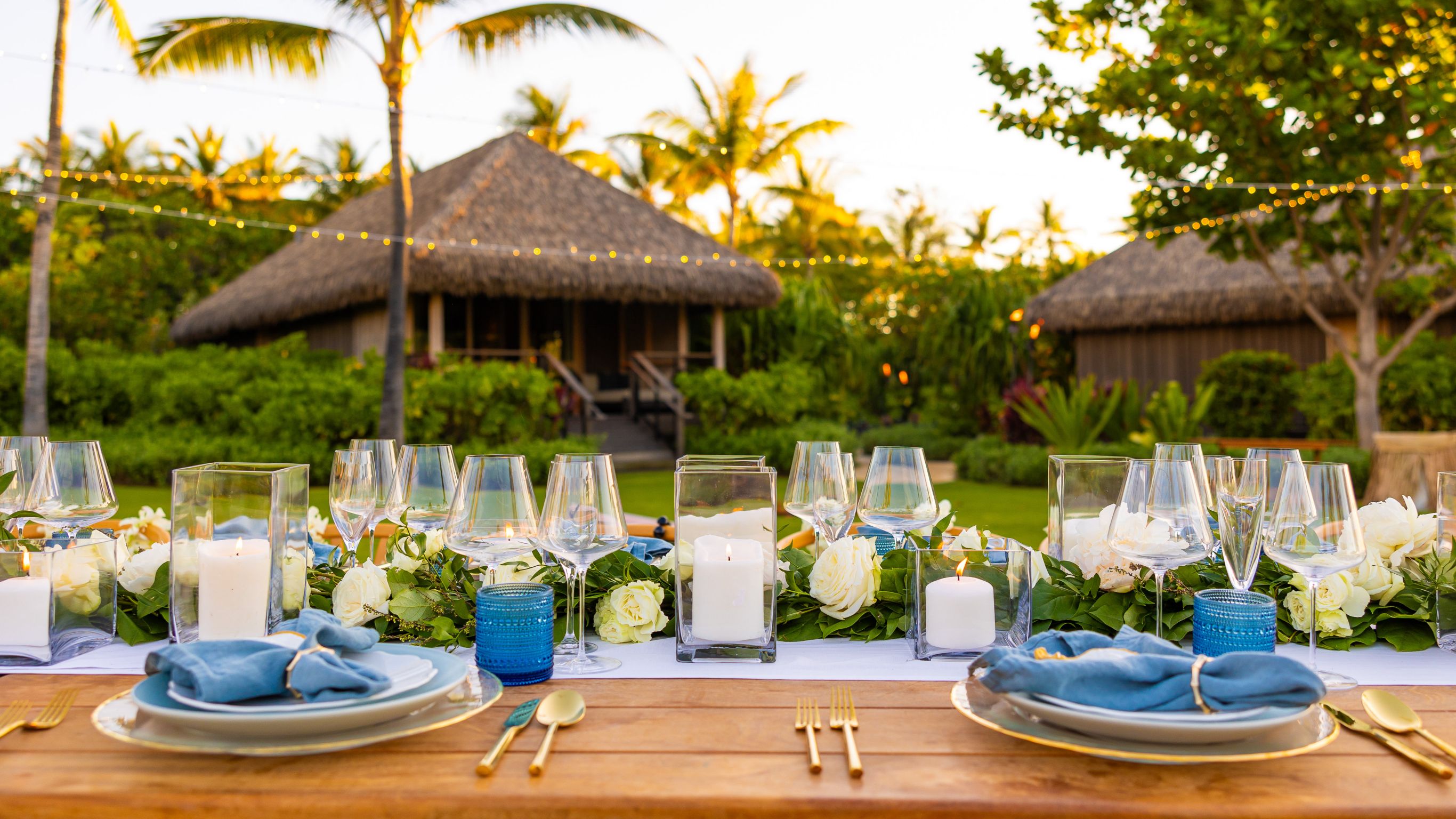 Wedding reception table in Hawaii with white candles, wine glasses, and blue napkins.
